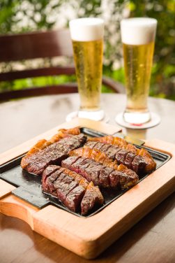 Tiras de carne na chapa servidas como petisco e acompanhadas por uma dupla de chopps