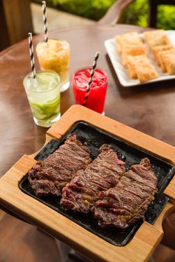 Tiras de carne na chapa servidas como petisco com pastéis e drinks
