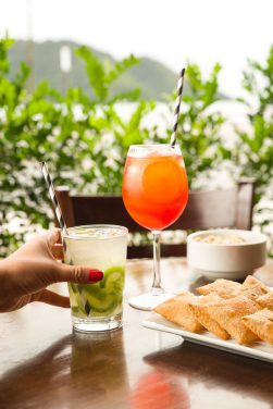 Porção de pastéis, aperol, caipirinha de limão sobre a mesa externa do Bar da Tertúlia com vista para o mar