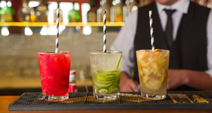 Três caipirinhas de diferentes frutas expostas no balcão.